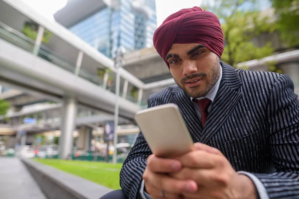 Indian businessman sitting outdoors in city while using mobile phone — Stock Photo, Image