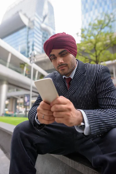 Indian businessman sitting outdoors in city while using mobile phone