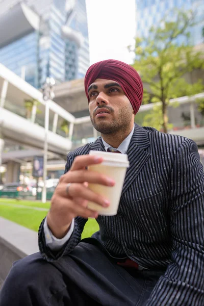 Indian businessman sitting outdoors in city while having coffee break