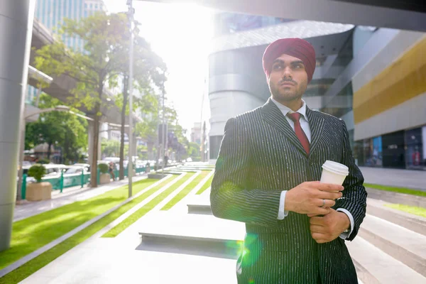 Indian businessman with turban outdoors in city holding coffee cup