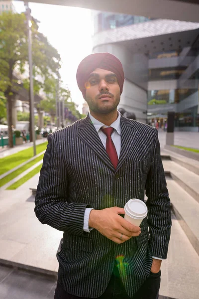 Indian businessman with turban outdoors in city holding coffee cup