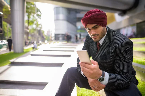 Indian businessman sitting outdoors in city while using mobile phone — Stock Photo, Image