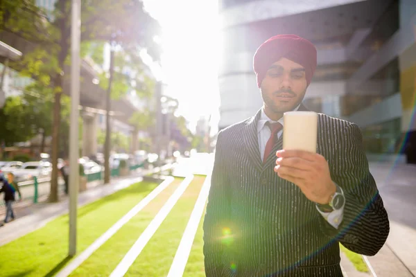 Indian businessman outdoors in city using phone with lens flare
