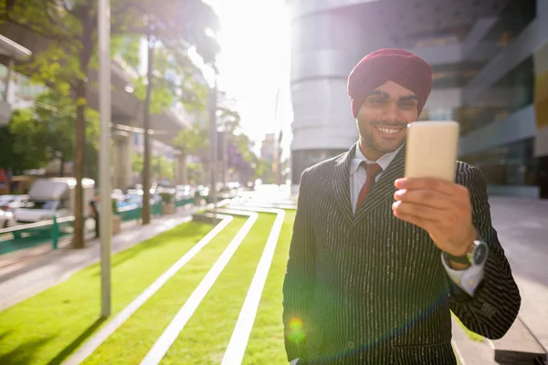 Indian businessman outdoors in city using phone with lens flare — Stock Photo, Image