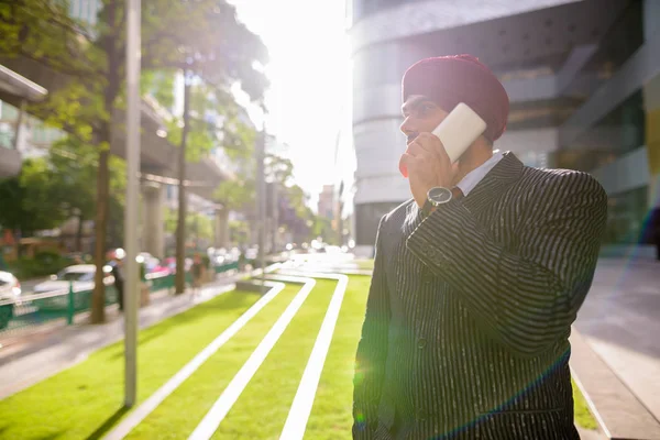 Indian businessman outdoors in city using phone with lens flare