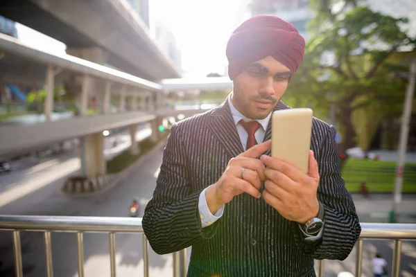 Indian businessman outdoors in city using phone with lens flare — Stock Photo, Image