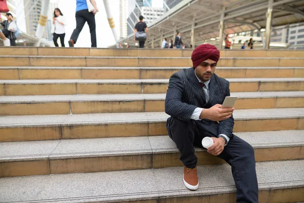 Homme d'affaires indien assis à l'extérieur en ville tout en utilisant le téléphone — Photo
