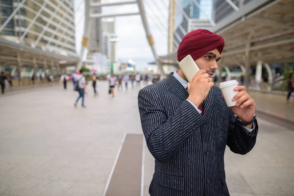 Indian businessman outdoors in city talking on phone and having coffee