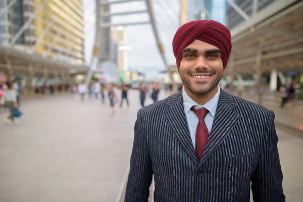 Portrait of happy Indian businessman with turban outdoors in city