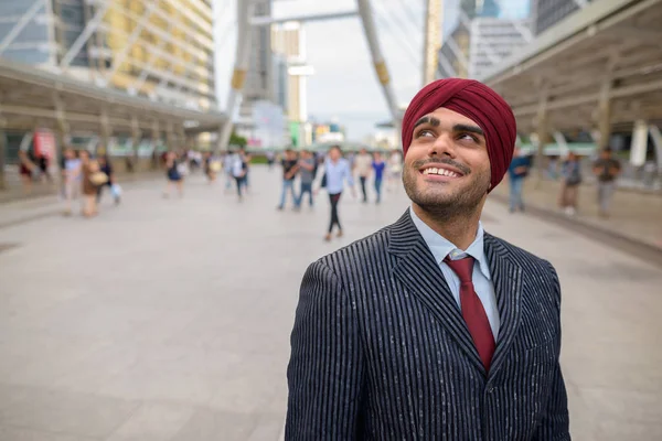 Happy Indian businessman with turban outdoors in city thinking