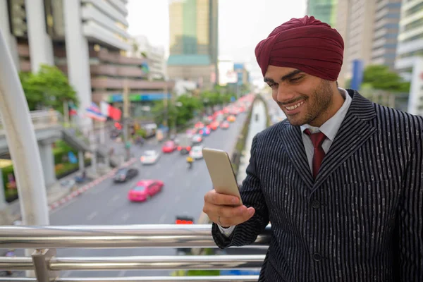 Indian businessman with turban outdoors in city using mobile phone