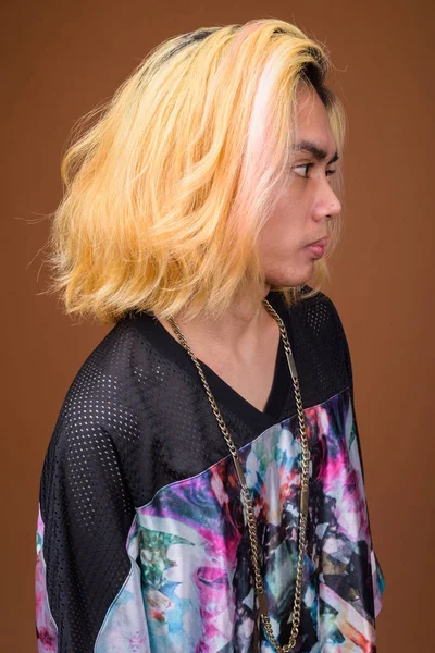 Pemuda Asia mengenakan pakaian bergaya terhadap latar belakang coklat — Stok Foto