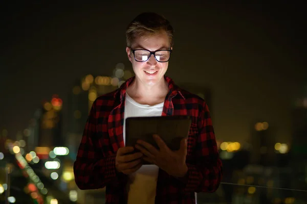 Ο άνθρωπος νεαρός ευτυχισμένη Hipster χρησιμοποιώντας ψηφιακή δισκίο κατά την άποψη της πόλης τη νύχτα — Φωτογραφία Αρχείου
