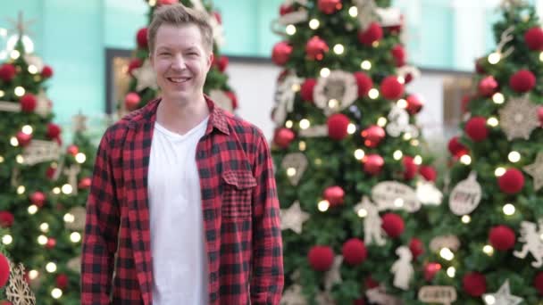 Feliz joven sonriendo contra árboles de Navidad iluminados al aire libre — Vídeo de stock