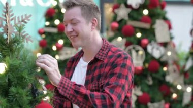 Açık havada Noel ağaçları bakarken gülümseyen genç mutlu Hipster adam