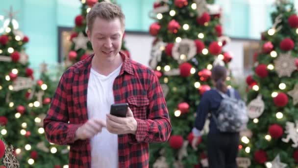 Gelukkig jonge Man met behulp van telefoon- en videogesprekken tegen kerst bomen buiten — Stockvideo