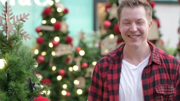 Feliz joven guapo hombre sonriendo contra los árboles de Navidad al aire libre — Vídeo de stock