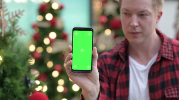 Joyeux jeune homme montrant téléphone contre les arbres de Noël éclairés à l'extérieur — Video