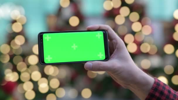 Rukou mladého muže pomocí telefonu proti osvětlené vánoční stromy venku — Stock video