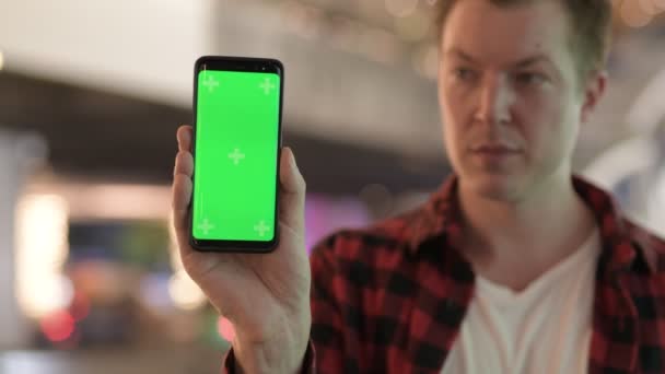 Feliz joven guapo hombre mostrando el teléfono en la ciudad por la noche — Vídeos de Stock