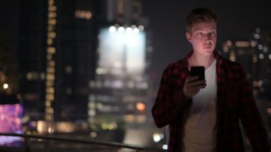 Yakışıklı delikanlı şehir manzarasına karşı telefonunuzun ve geceleri