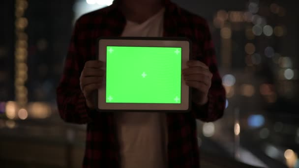 Joven mostrando tableta digital contra vista de la ciudad por la noche — Vídeo de stock