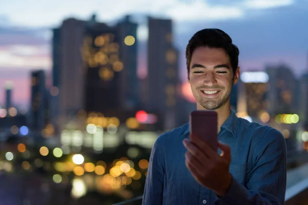 Πορτρέτο του ανθρώπου σε εξωτερικούς χώρους το βράδυ στην πόλη χρησιμοποιώντας κινητό τηλέφωνο — Φωτογραφία Αρχείου