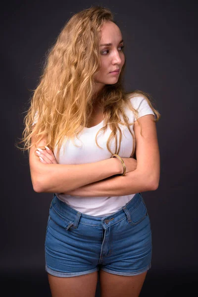 Νεαρή όμορφη γυναίκα με μακριά κυματιστά ξανθά μαλλιά εναντίον γκρι bac — Φωτογραφία Αρχείου