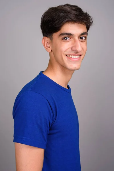 Fiatal boldog perzsa tizenéves fiú mosolyogva sötétszürke háttérrel — Stock Fotó