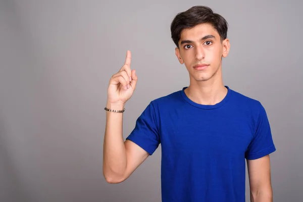 Jovem bonito adolescente persa apontando o dedo para cima contra fundo cinza — Fotografia de Stock