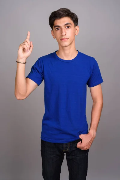 Jovem bonito adolescente persa apontando o dedo para cima contra fundo cinza — Fotografia de Stock