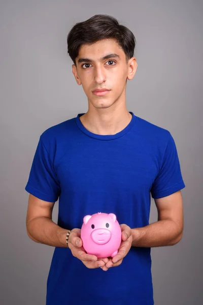 돼지 저금통을 들고 젊은 잘생긴 페르시아어 십 대 소년 — 스톡 사진