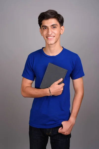 Young handsome Persian teenage boy student holding book — Stock Photo, Image