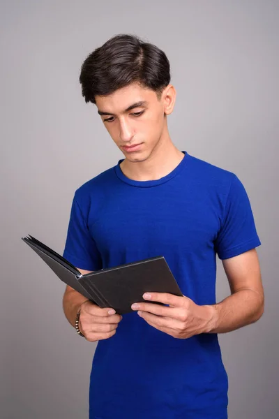 Young handsome Persian teenage boy student holding book — Stock Photo, Image