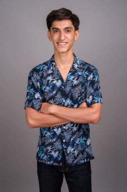 Stüdyoda, gri arka planda Hawaii tişörtü giyen genç, yakışıklı İranlı bir çocuk görülüyor.