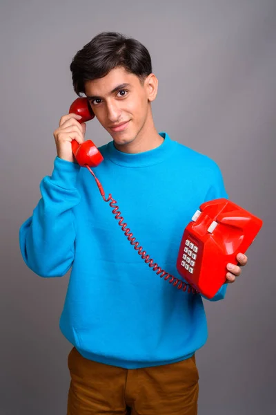 Young handsome Persian teenage boy talking on red old phone — Stock Photo, Image