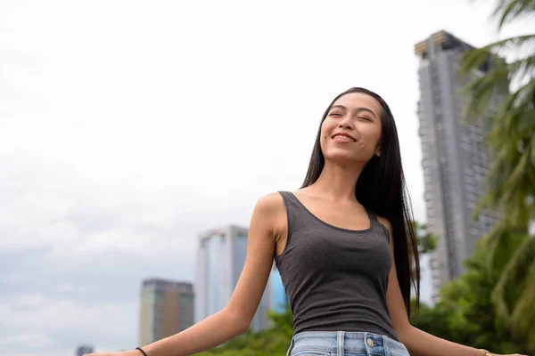 Boldog fiatal gyönyörű ázsiai nő pihentető a parkban, a szeme zárva — Stock Fotó