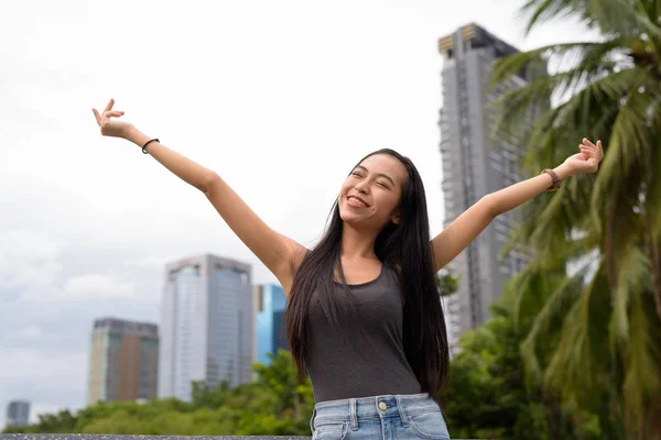 Joven hermosa mujer asiática relajándose en el parque con los brazos levantados —  Fotos de Stock
