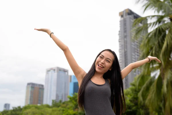 Jeune belle femme asiatique se détendre au parc avec les bras levés — Photo