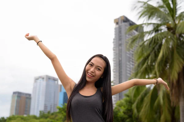 Junge schöne asiatische Frau entspannt sich im Park mit erhobenen Armen — Stockfoto
