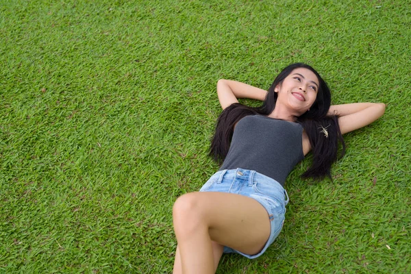 Mutlu genç güzel Asyalı kadın parkta çimlere bırakmasını — Stok fotoğraf