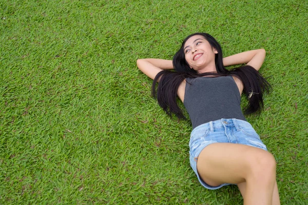 Feliz joven hermosa mujer asiática acostada en la hierba en el parque —  Fotos de Stock