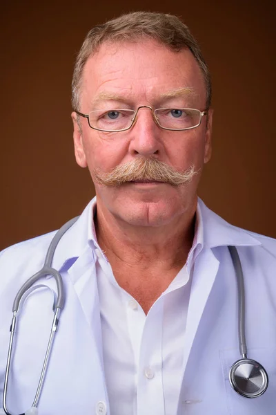 Volto di anziano uomo medico con baffi contro marrone backgroun — Foto Stock