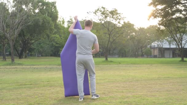 Jonge knappe man opzetten van yoga mat in het park — Stockvideo