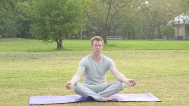 Fiatal jóképű férfi pihentető, miközben meditál a parkban — Stock videók