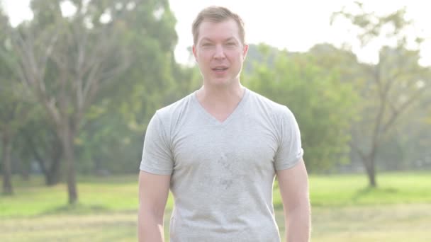 Boldog jóképű fiatalember beszél a parkban — Stock videók