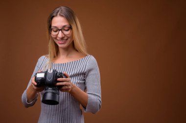 Kahverengi arka planı DSLR kamera tutan genç güzel kadın fotoğrafçı