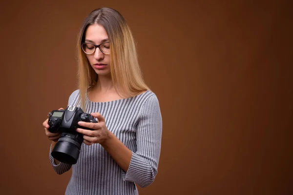 Νεαρή όμορφη γυναίκα φωτογράφος κατέχουν Dslr φωτογραφική μηχανή καφέ φόντο — Φωτογραφία Αρχείου