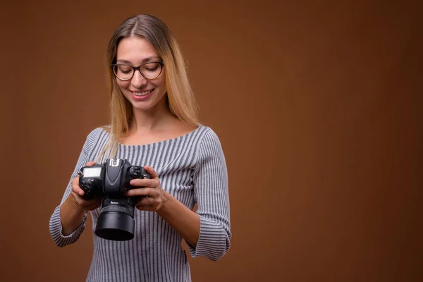 Mooie jongedame fotograaf Dslr camera houden tegen bruine achtergrond — Stockfoto