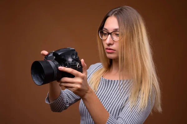 年轻的美丽的女摄影师拿着 dslr 照相机在棕色背景 — 图库照片